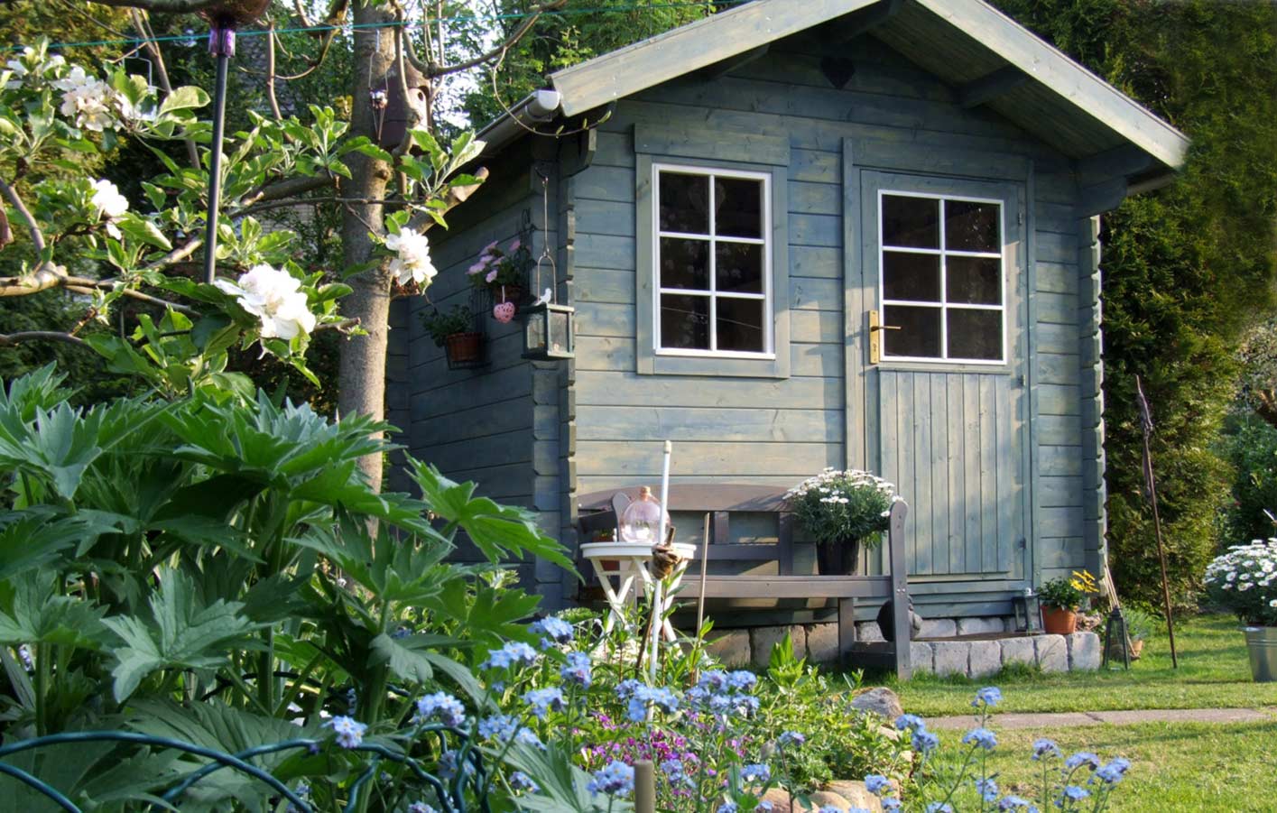 Gartenhaus mit Holzverkleidung und gepflegtem Garten im Hintergrund.